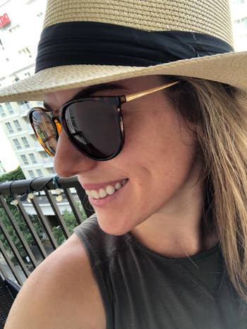 Person smiling in sunglasses and a straw hat on a balcony, suggesting a relaxed, summery vibe