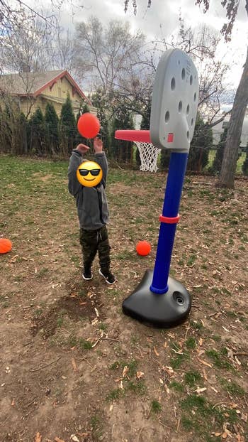 Child playing with a basketball and a toy hoop in a backyard