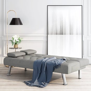 the gray futon laying flat with a blue throw blanket tossed on it