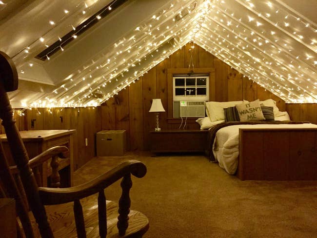 a reviewer photo of an attic bedroom with the string lights installed along the ceiling 