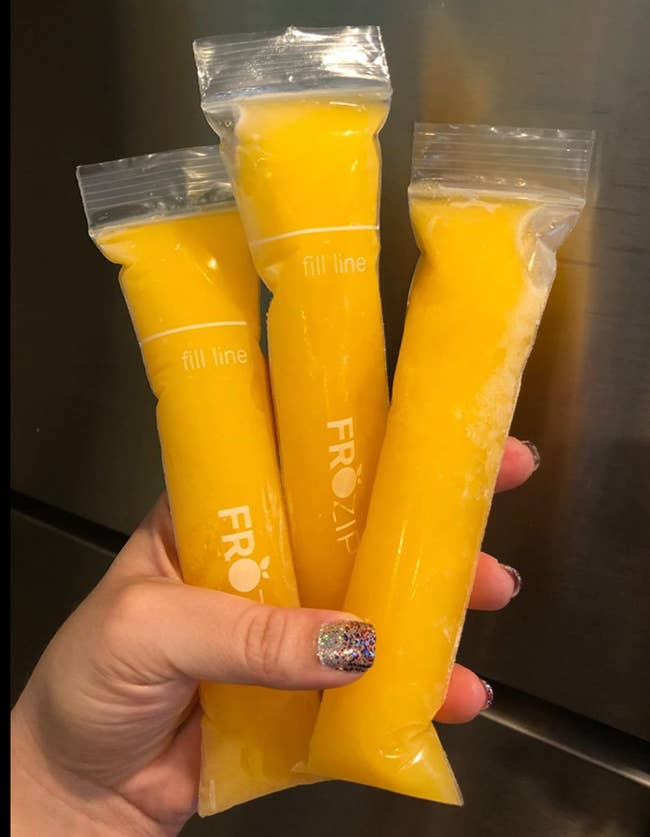 Reviewer holding up frozen orange juice pops in narrow plastic bags 