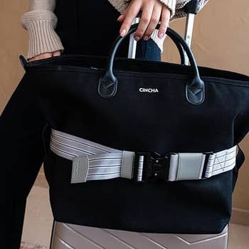 the belt in gray wrapped around a black tote on top of a suitcase 