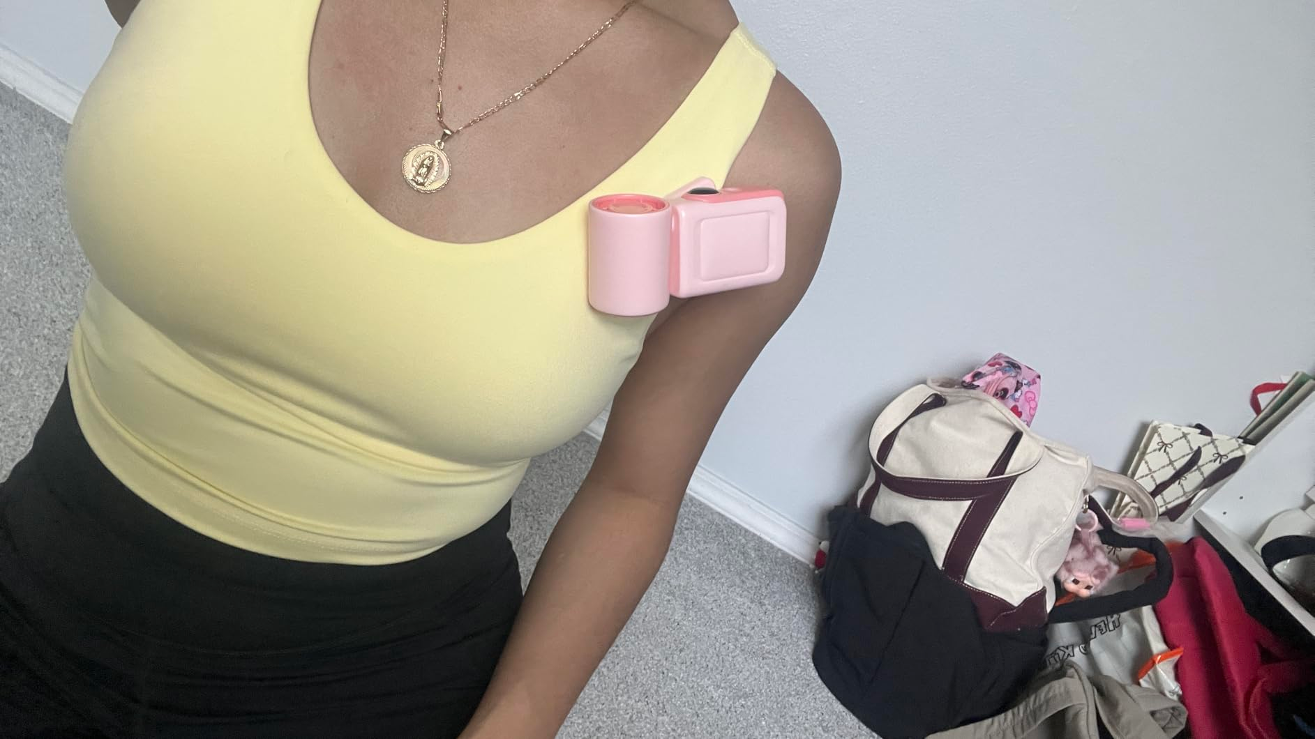 Person successful  a sleeveless apical  showcases a pinkish  portable instrumentality   clipped to their shoulder. Background includes bags connected  the floor