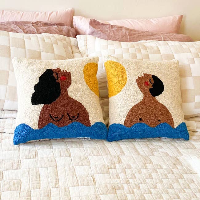two hook pillows, one with a pattern of a person with long hair and breasts swimming while starting at the sun. the second pillow is of a person with short hair mimicking the look.