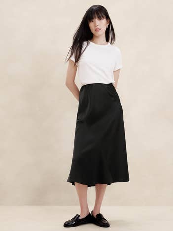 Model in a plain white tee and black midi skirt with loafers