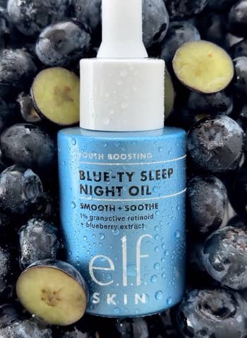 Blue vessel  of e.l.f. Skin's Blue-ty Sleep Night Oil among blueberries, labeled for younker  boosting and smoothing with granactive retinoid and blueberry extract