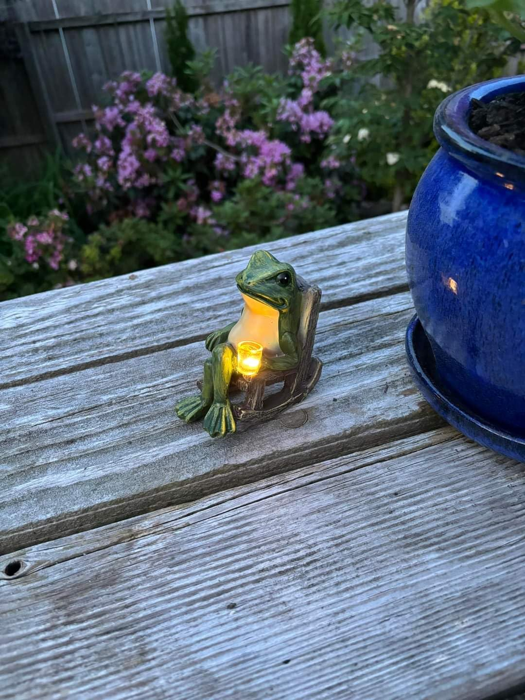 A small frog figurine holding a glowing coffee cup light light and sitting on wooden rocking chair