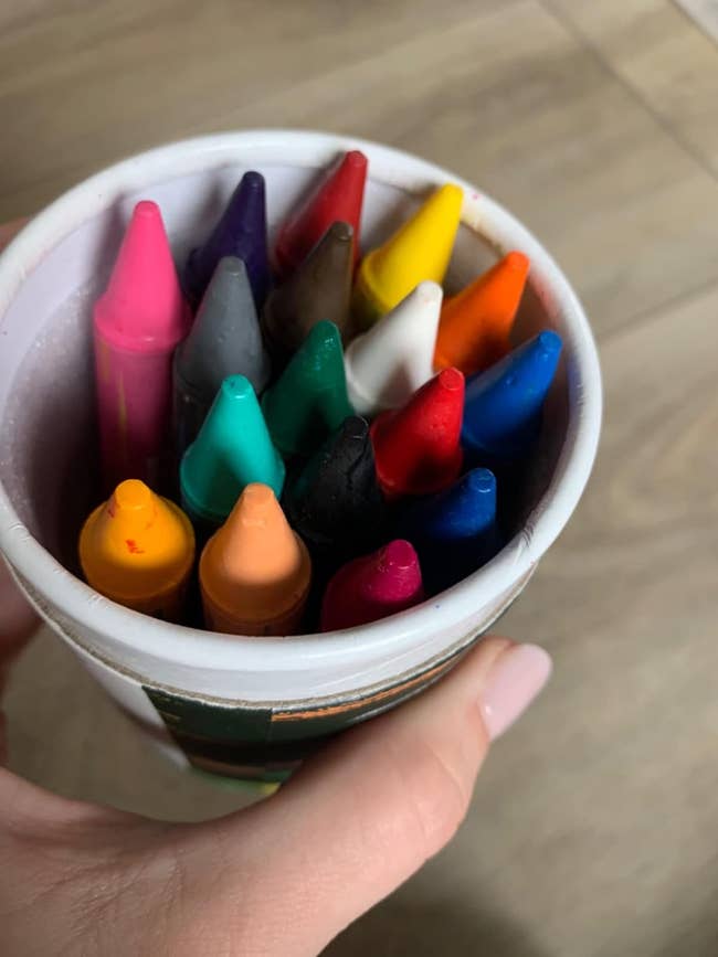 Hand holding a cup filled with assorted crayons, useful for creative projects or coloring