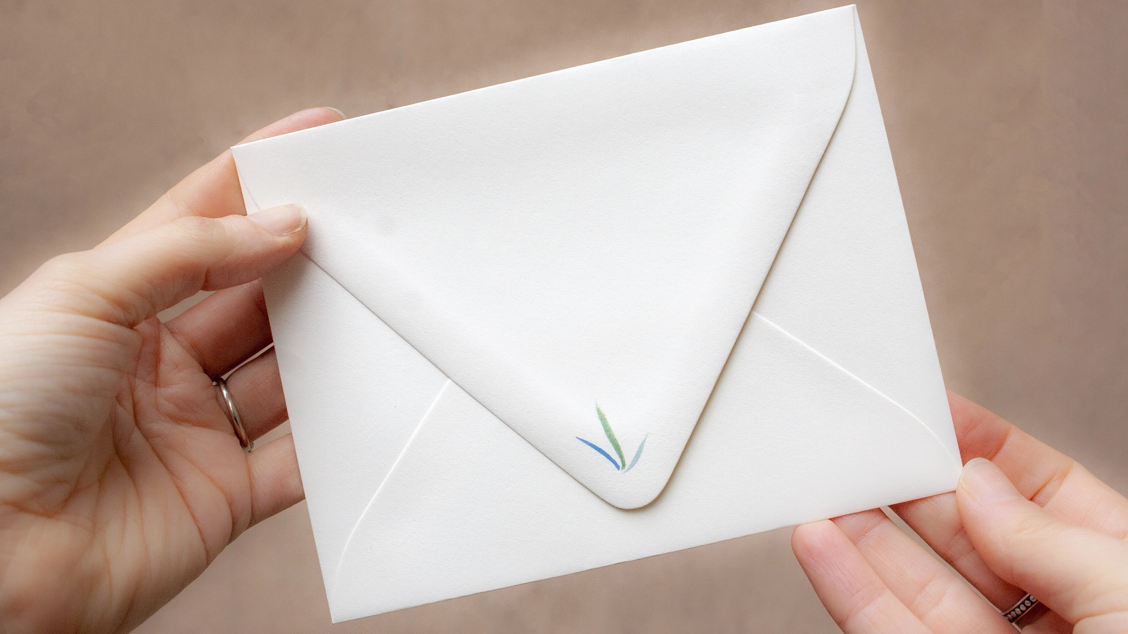 Hands holding a sealed envelope with a small blue and green logo on the flap