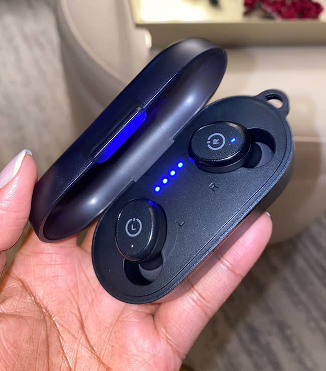 reviewer holding black earbuds in charging case