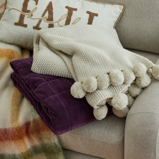 Knitted broad  with ample  pom-poms draped implicit    a plush purple propulsion  connected  a couch, with a 