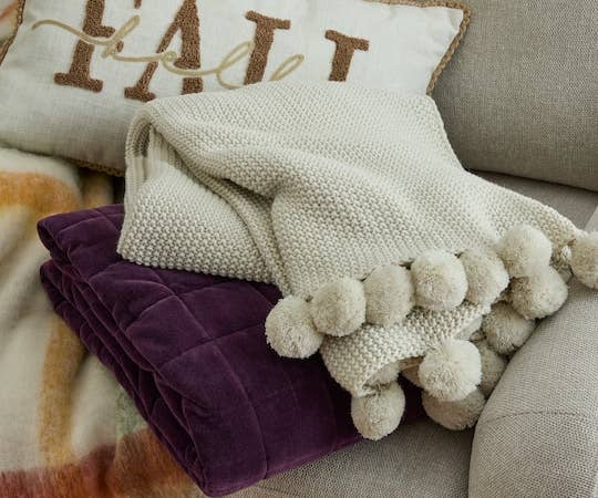 Knitted broad with ample pom-poms draped implicit a plush purple propulsion connected a couch, with a