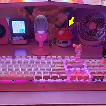 Desk with backlit keyboard, microphone, decorative items, and mini fan. Yellow arrow pointing to a detail