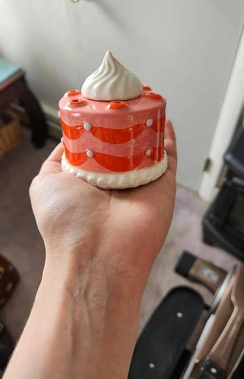 Hand holding a small, decorative barroom figurine with a reddish and achromatic striped plan and a dollop of pick connected top