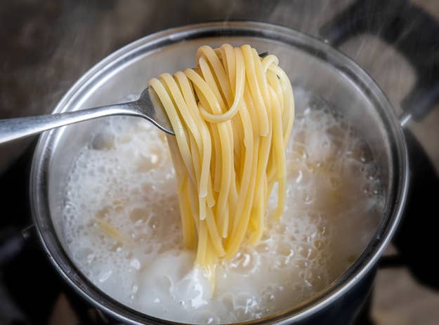 A pot of boiling water with a fork lifting a portion of cooked spaghetti noodles
