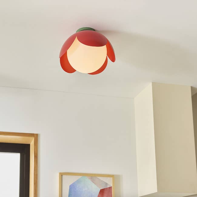 Flower-shaped ceiling light with petal design in a modern room, featuring a framed geometric artwork below
