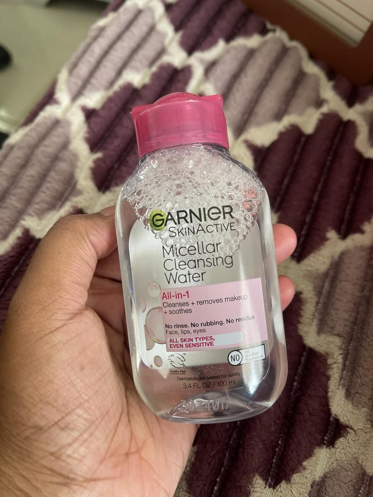 Hand holding a bottle of Garnier SkinActive Micellar Cleansing Water on a patterned surface