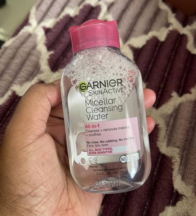 Hand holding a bottle of Garnier SkinActive Micellar Cleansing Water on a patterned surface