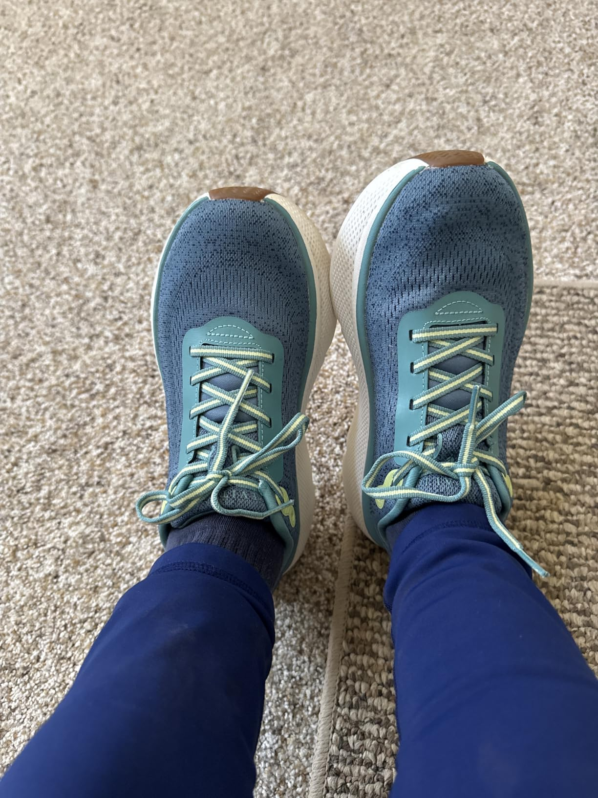 Person wearing teal athletic shoes with laces and blue leggings on a carpeted floor, showcasing casual footwear for shopping