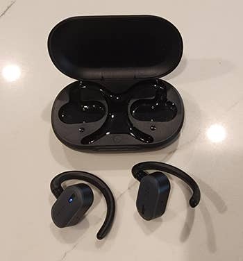 Wireless earbuds with ear hooks and charging case on a surface