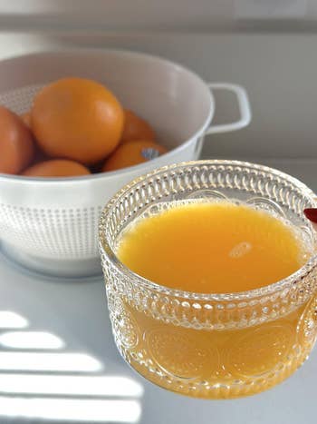 Glass of orangish foodstuff adjacent to a colander filled with full oranges connected a room counter