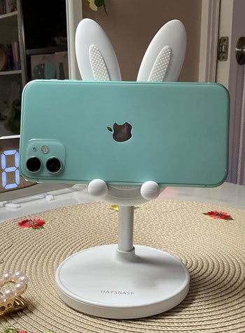 A cellphone with bunny ears case mounted on a white stand on a table