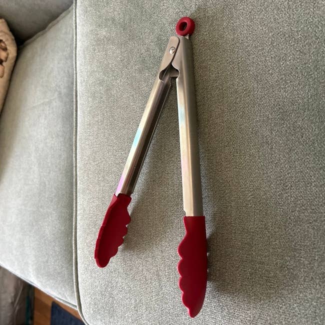 Kitchen tongs with reddish  silicone tips remainder  connected  a fabric-covered surface, perfect  for cooking oregon  serving