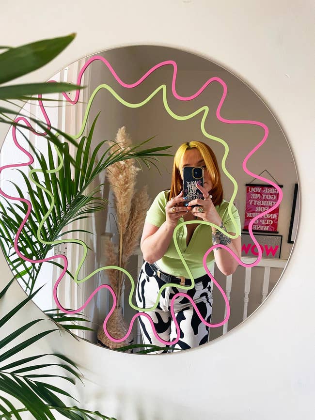 model posing in circle mirror with green and pink squiggle design