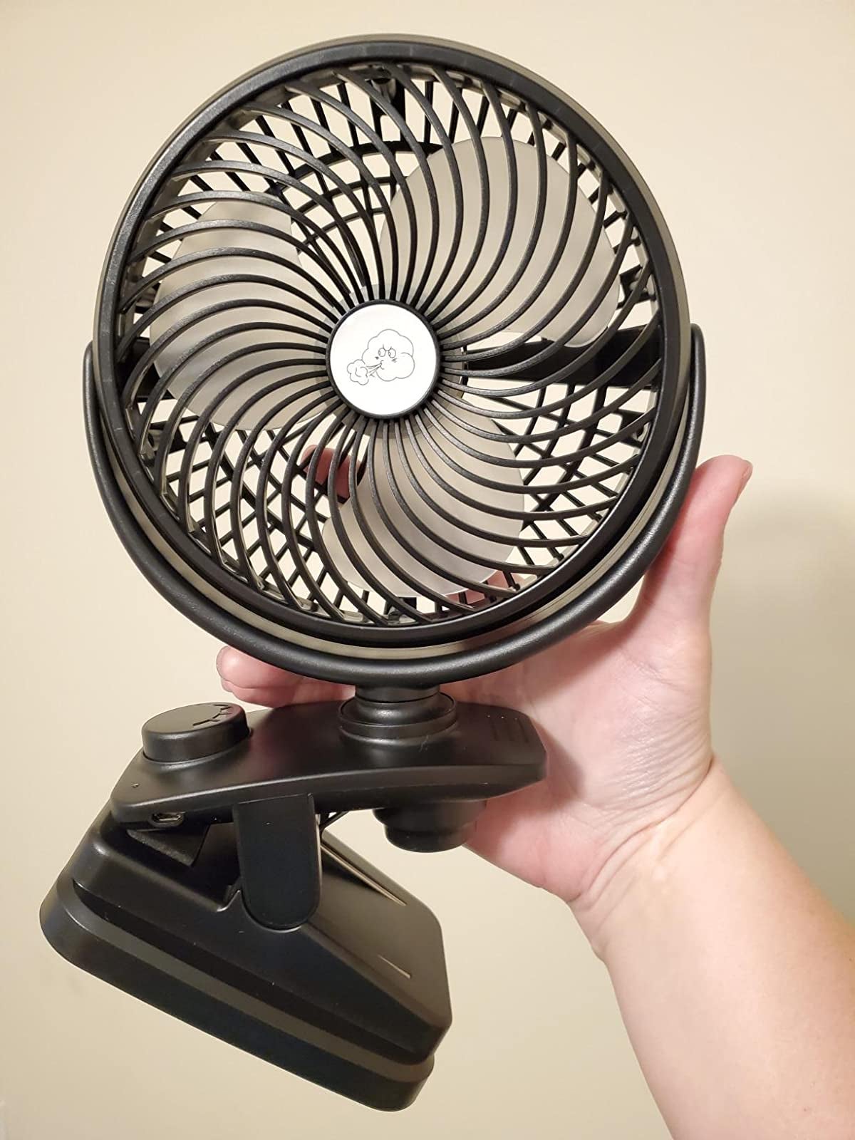 Reviewer holding black battery powered fan with clamp attached