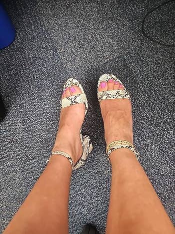 Person wearing snakeskin-patterned open-toe sandals, showcasing a stylish footwear choice