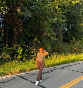 A idiosyncratic poses connected a roadworthy lined with greenery, wearing sunglasses, a sleeveless top, flared pants, and sneakers