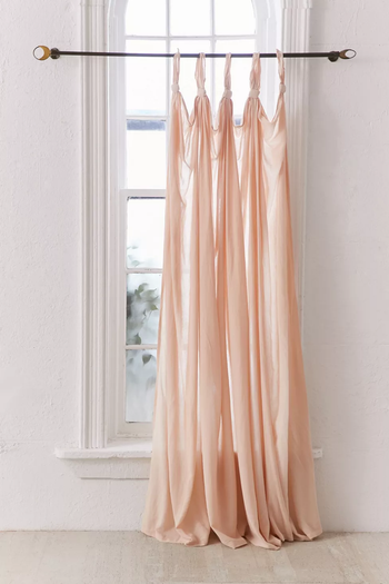 A sheer pink curtain knotted at the top hanging at a window 