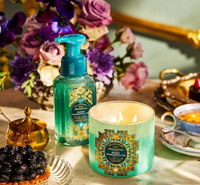 A candle and hand soap from Charlotte's Tea collection on a table with flowers and tea accessories