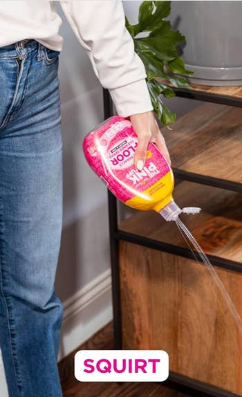 Person utilizing pinkish  cleaning solution   vessel  to squirt liquid connected  woody  furniture, with 