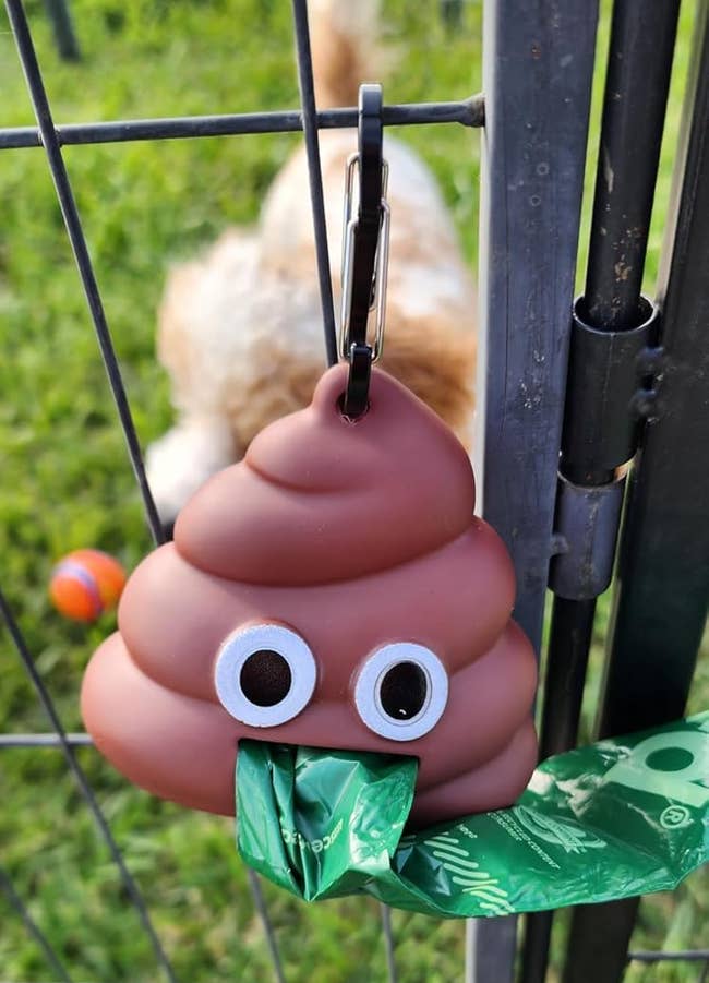 Cute poop emoji container holder with canine discarded bags attached, hanging connected a fence. Dog disposable done the fence