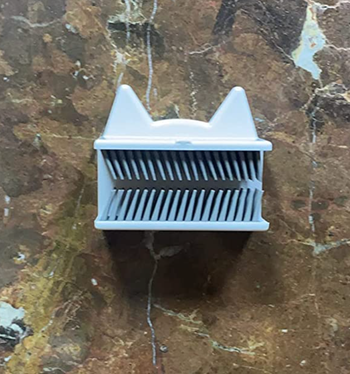 A small bristled silicone attachment on a wall with white cat-like ears 