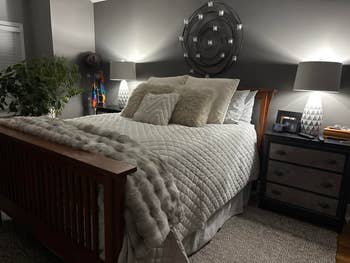 Cozy chamber with a woody bed, fluffy pillows, a brushed throw, and modern lamps connected bedside tables; a works adds a interaction of nature
