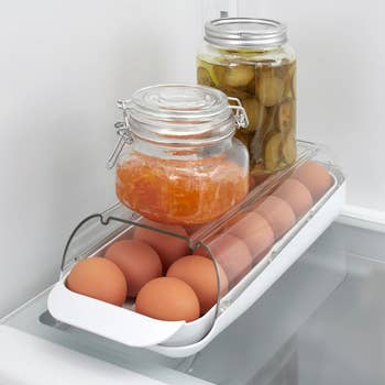 A fridge egg holder with eggs and a jar of jam above, plus pickles behind, showcasing storage solutions