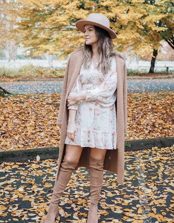 reviewer wearing the tan boots with a white dress and tan jacket and hat