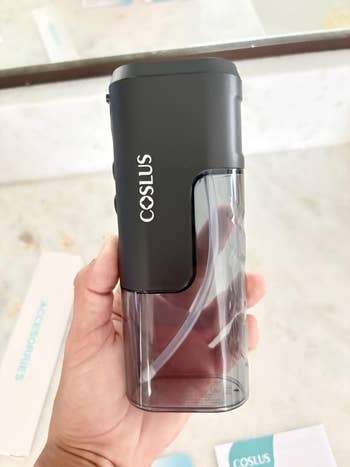 Hand holding a portable flosser with a sleek plan and the marque sanction