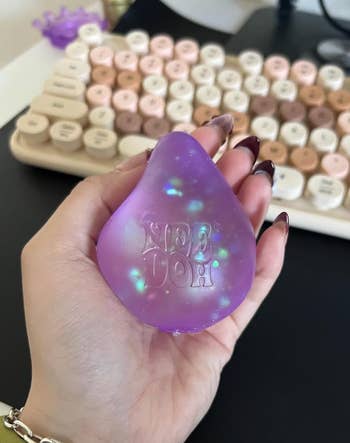 Hand holding an iridescent stress ball labeled 