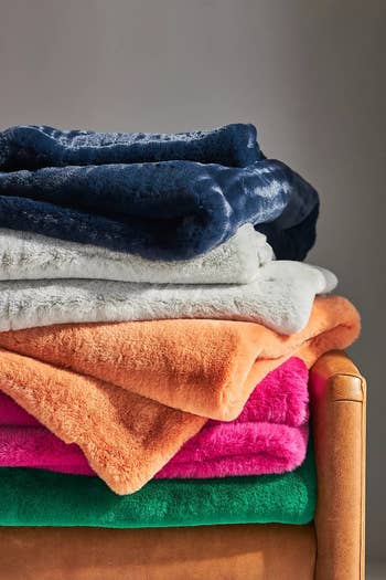 a stack of blankets, one navy, one gray, one orange, one magenta