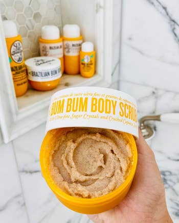 modelholding an unfastened jar of Sol de Janeiro Bum Bum Body Scrub