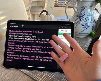 reviewer wearing the pink remote as a ring with their hand in front of their tablet, which has song lyrics on its screen