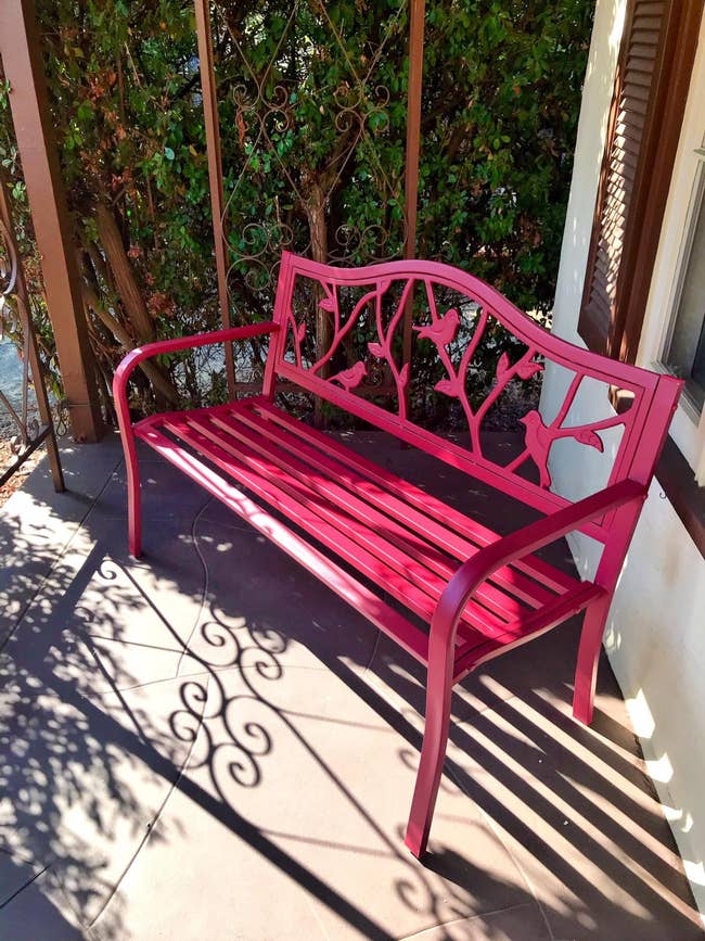 reviewer's red metal garden bench with decorative bird design on backrest