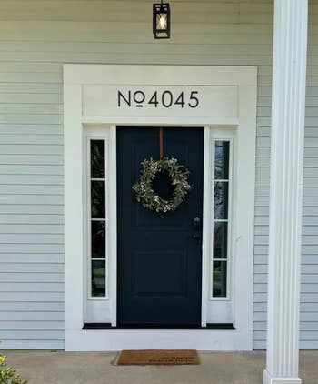 Black front door with decorative wreath and house number 