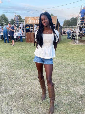 Reviewer in a casual white top and denim shorts paired with brown cowboy boots at an outdoor event