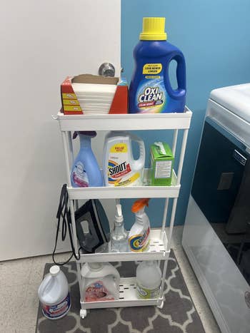 A achromatic  shelving portion   holds assorted  laundry and cleaning products, including detergent, cloth  softener, and stain removers
