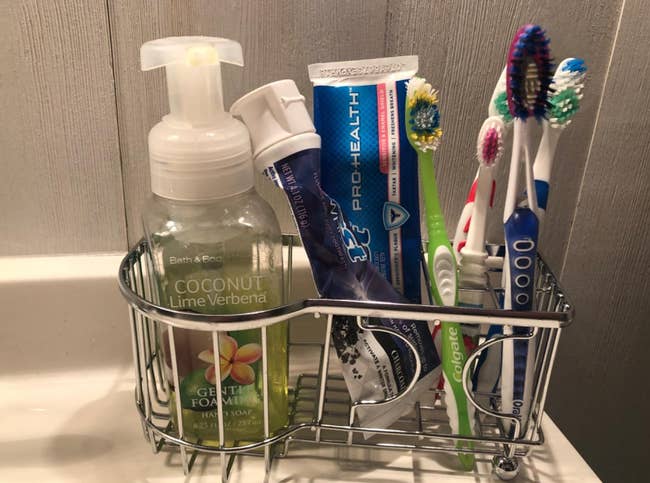 a reviewer photo of the toothbrush holder filled with four toothbrushes, two tubes of toothpaste, and a bottle of hand soap 