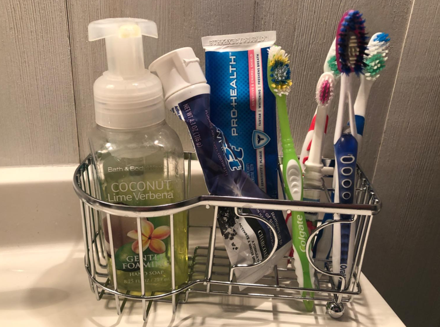 a reviewer photo of the toothbrush holder filled with four toothbrushes, two tubes of toothpaste, and a bottle of hand soap 
